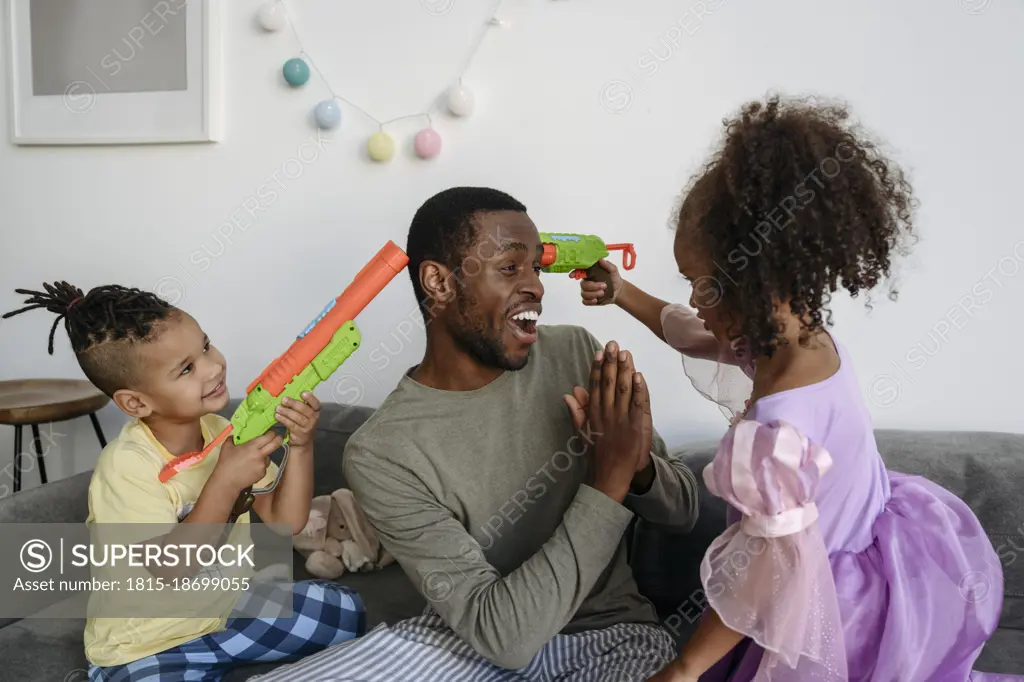 Children with squirt guns pointing at father in living room
