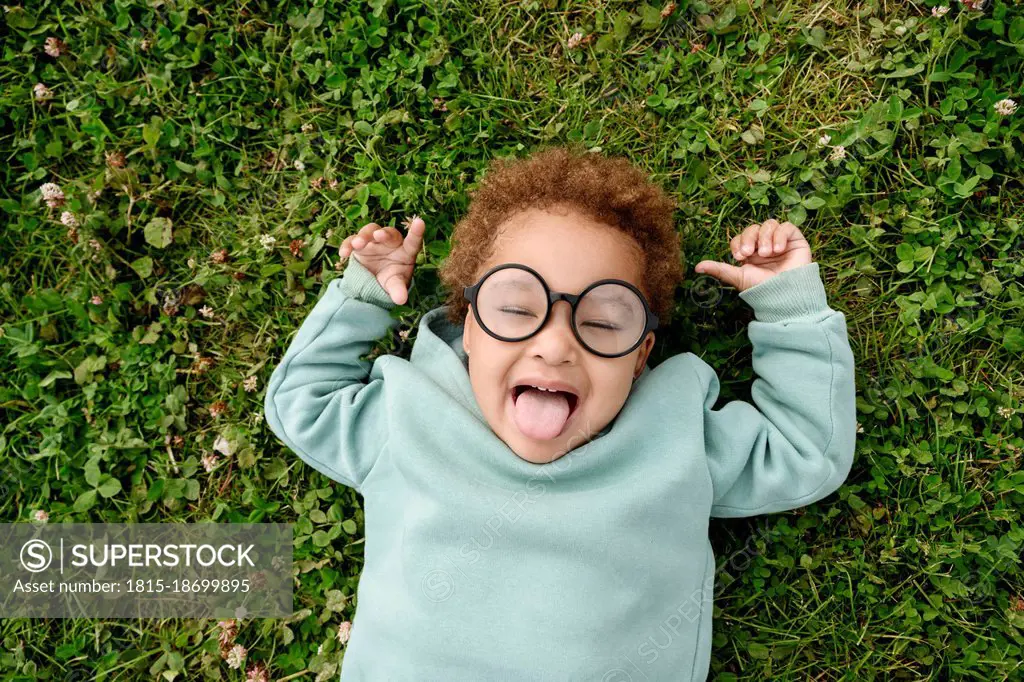 Cute girl with eyeglasses sticking out tongue on grass