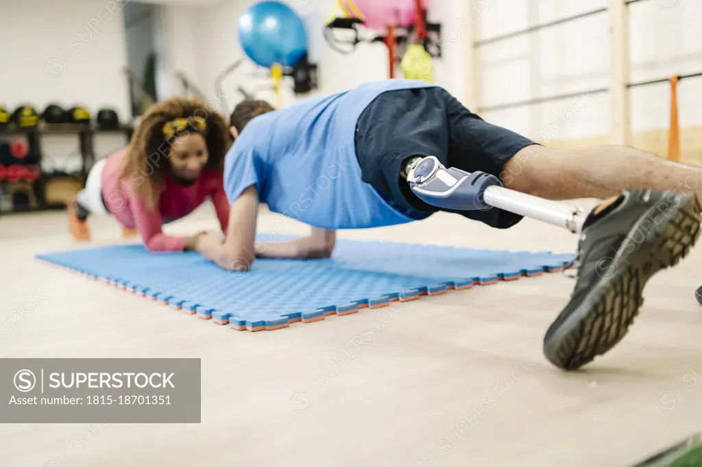 Sportsman with disability practicing plank position with friend on mat in gym