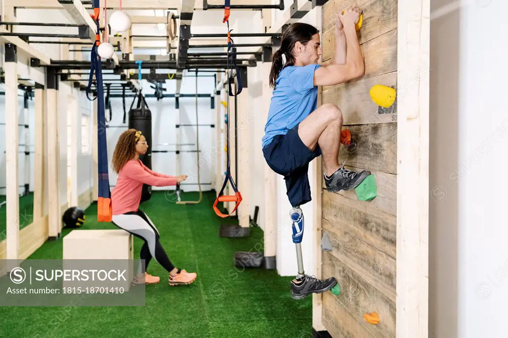 Disabled sportsman climbing wall in gym