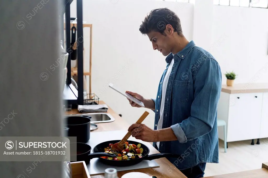 Man using digital tablet while preparing food in kitchen