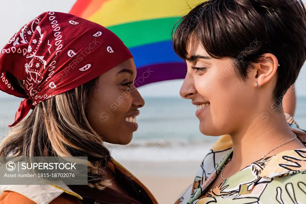 Romantic lesbian couple with rainbow flag staring each other at beach