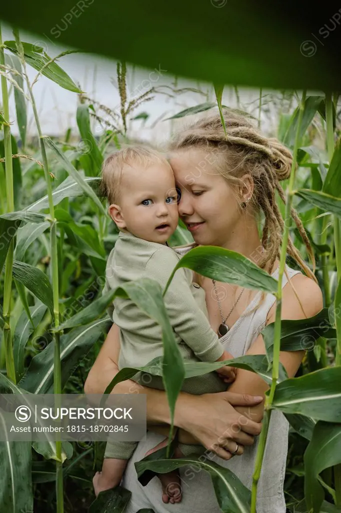 Mother with eyes closed embracing toddler in corn field