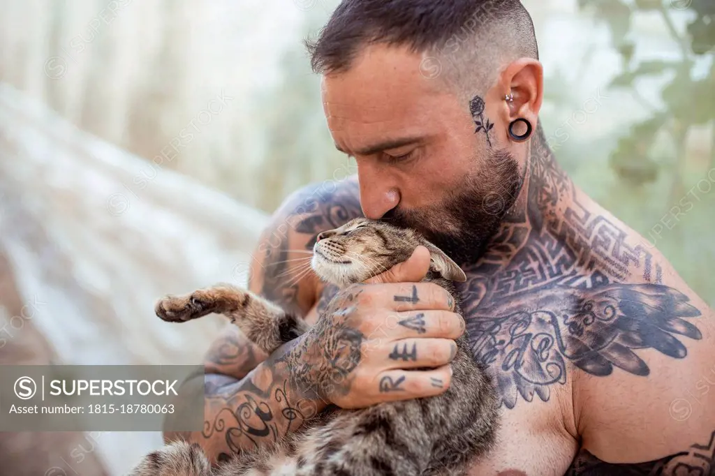 Shirtless man with tattoo kissing cat