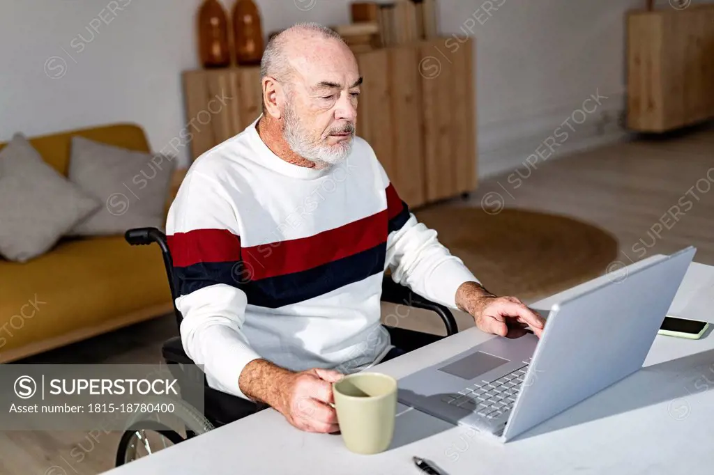 Disabled businessman with coffee cup using laptop at home office