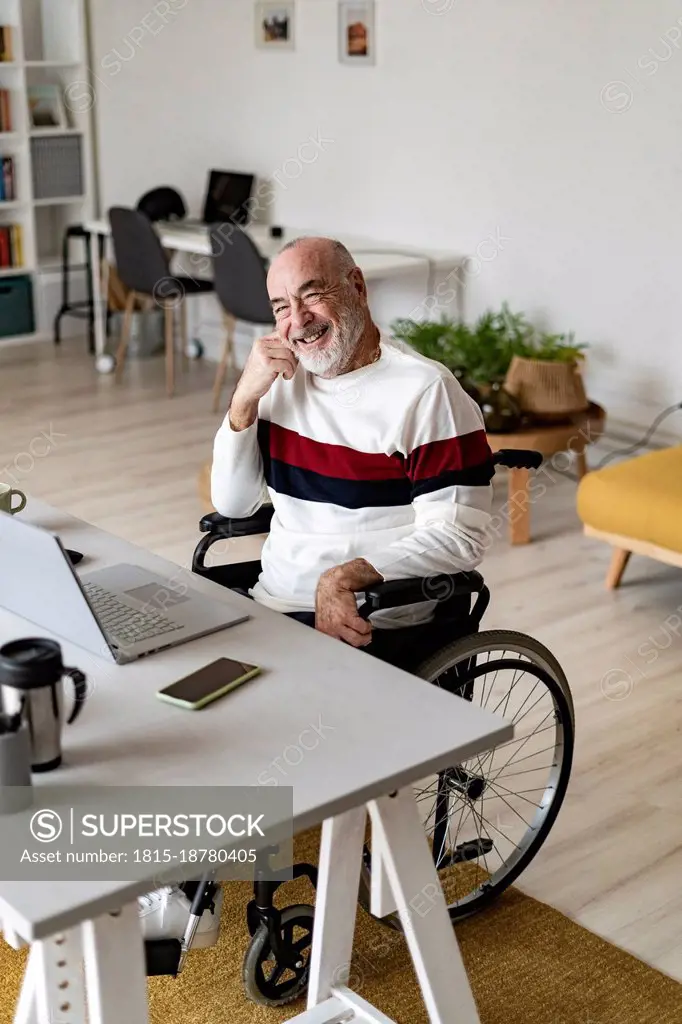 Smiling senior businessman sitting on wheelchair at home office
