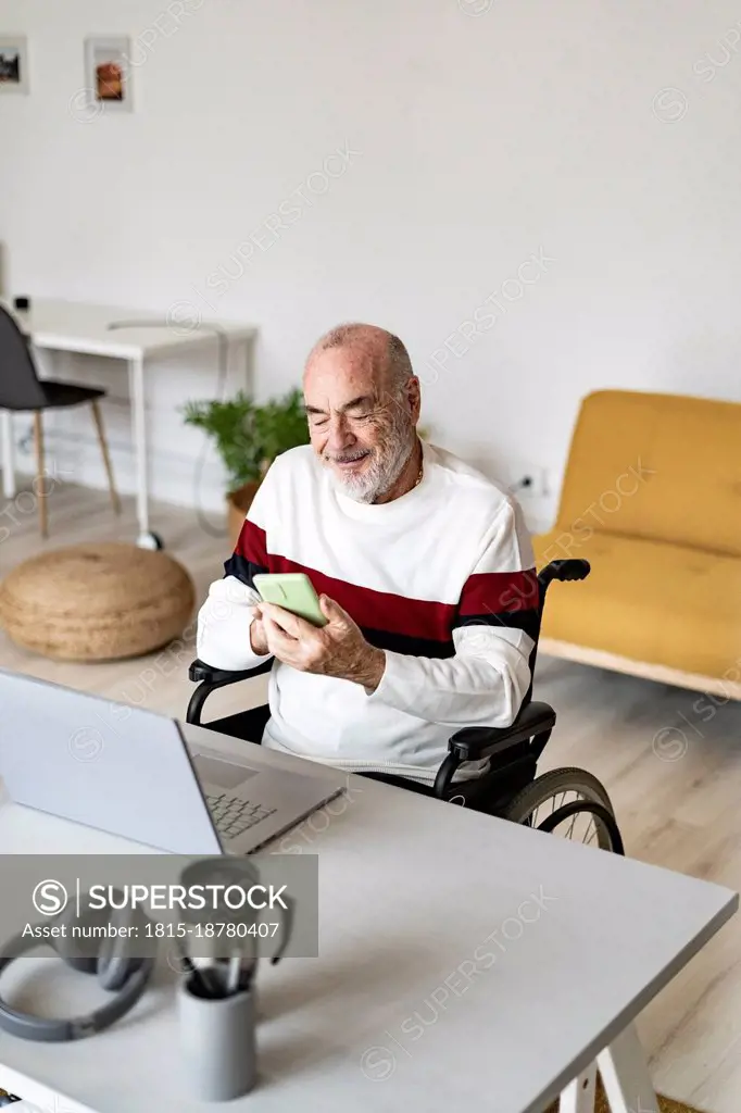 Senior businessman on wheelchair using mobile phone at home office