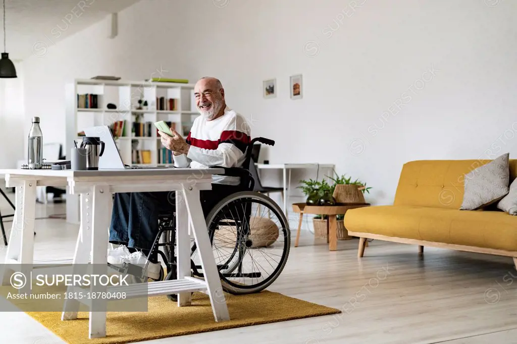 Senior disabled businessman with mobile phone and laptop at home office