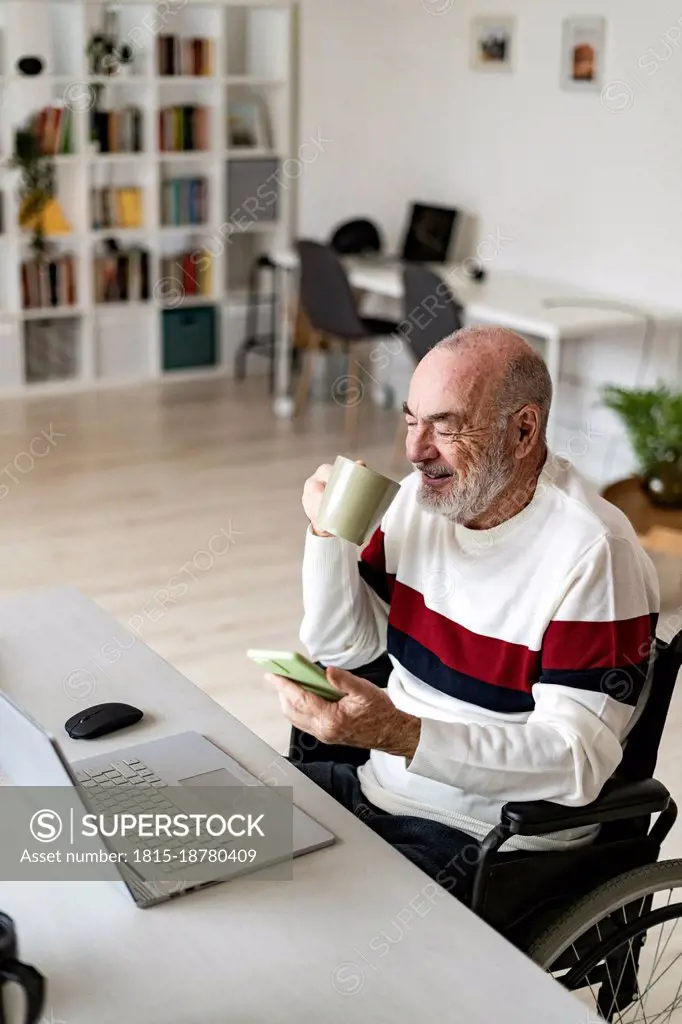 Businessman with mobile phone having coffee at home office