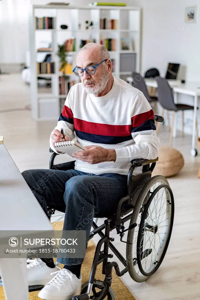 Businessman with physical disability writing on note pad at home