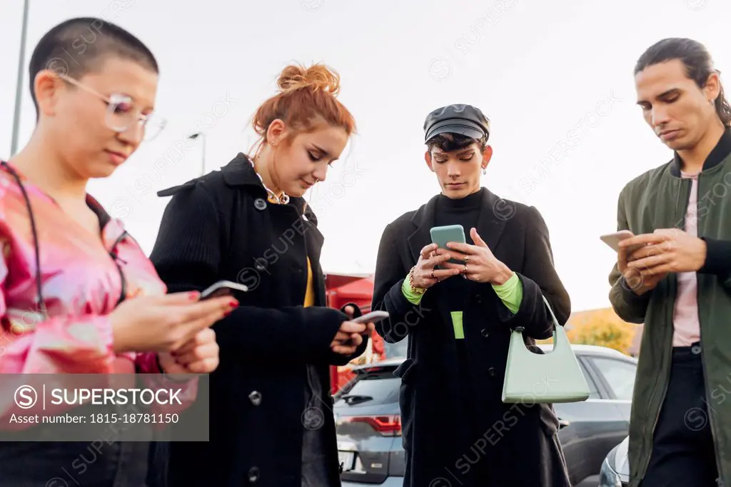 Friends wearing jacket using mobile phones at parking lot
