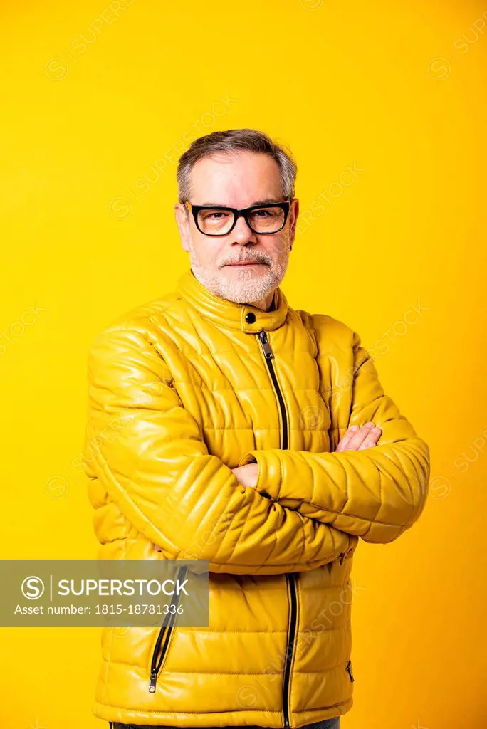 Confident man with arms crossed against yellow background