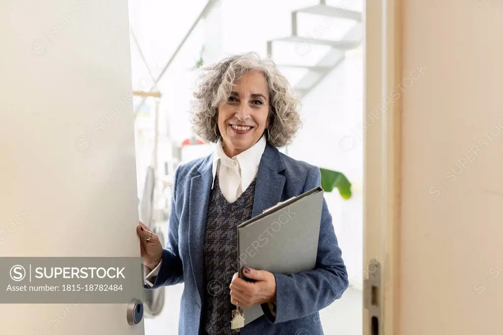 Smiling real estate agent with file standing on doorway at apartment