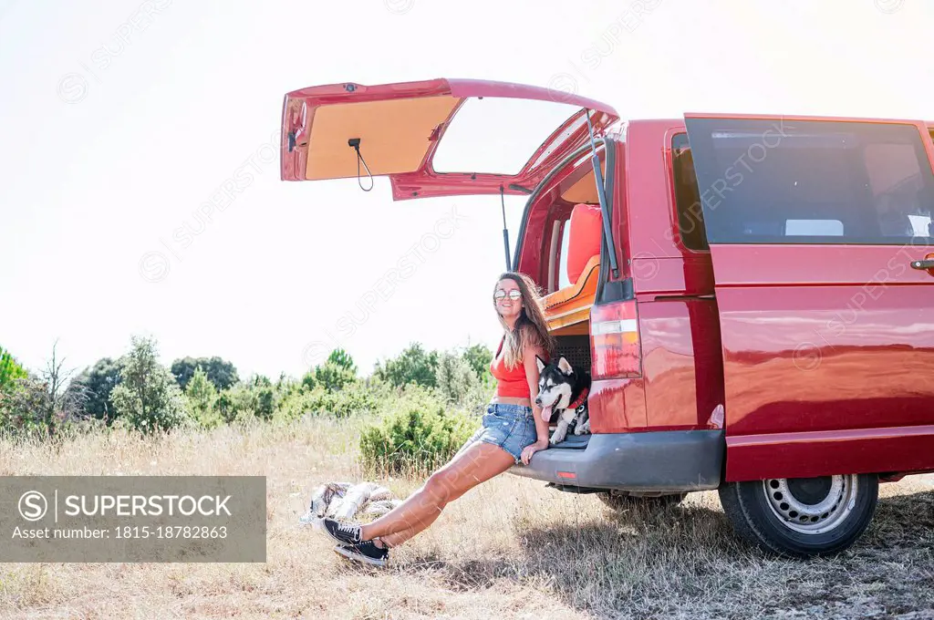 Woman sitting by dog in van trunk on road trip