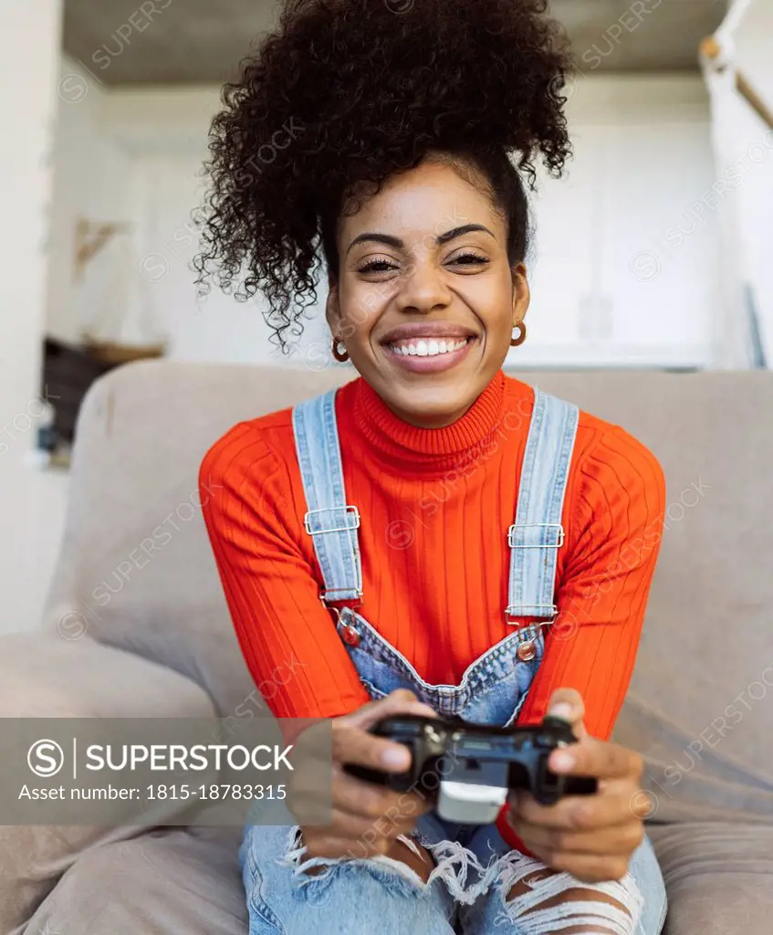 Happy curly haired woman playing video game on sofa