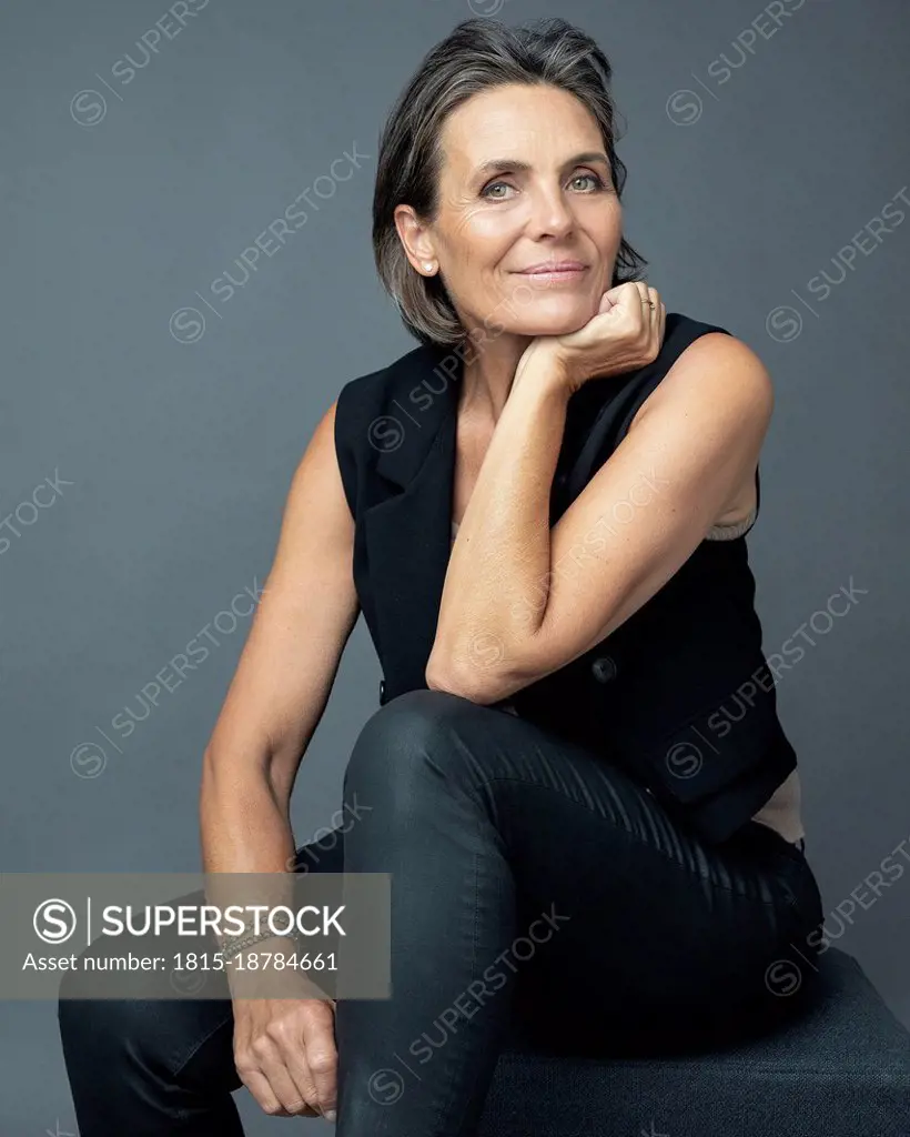 Smiling woman with hand on chin sitting against gray background