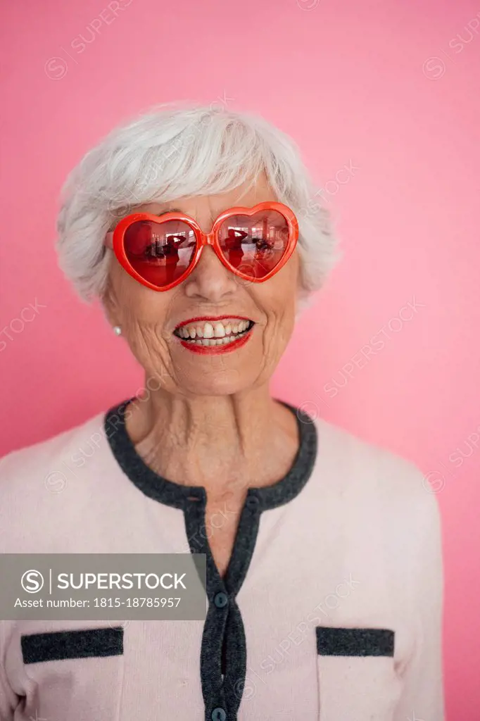 Happy woman with heart shape sunglasses against pink background