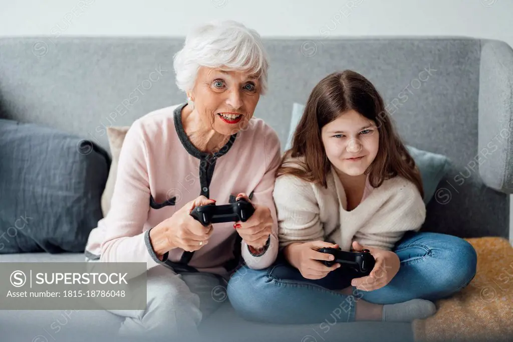 Grandmother playing video game with granddaughter at home