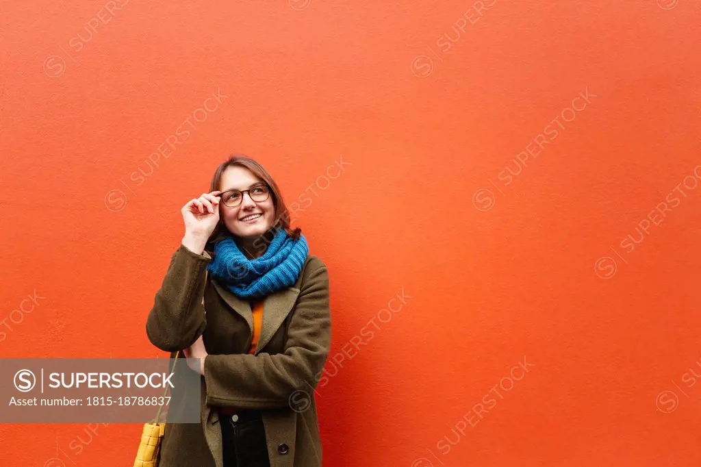 Smiling woman wearing eyeglasses in front of orange wall