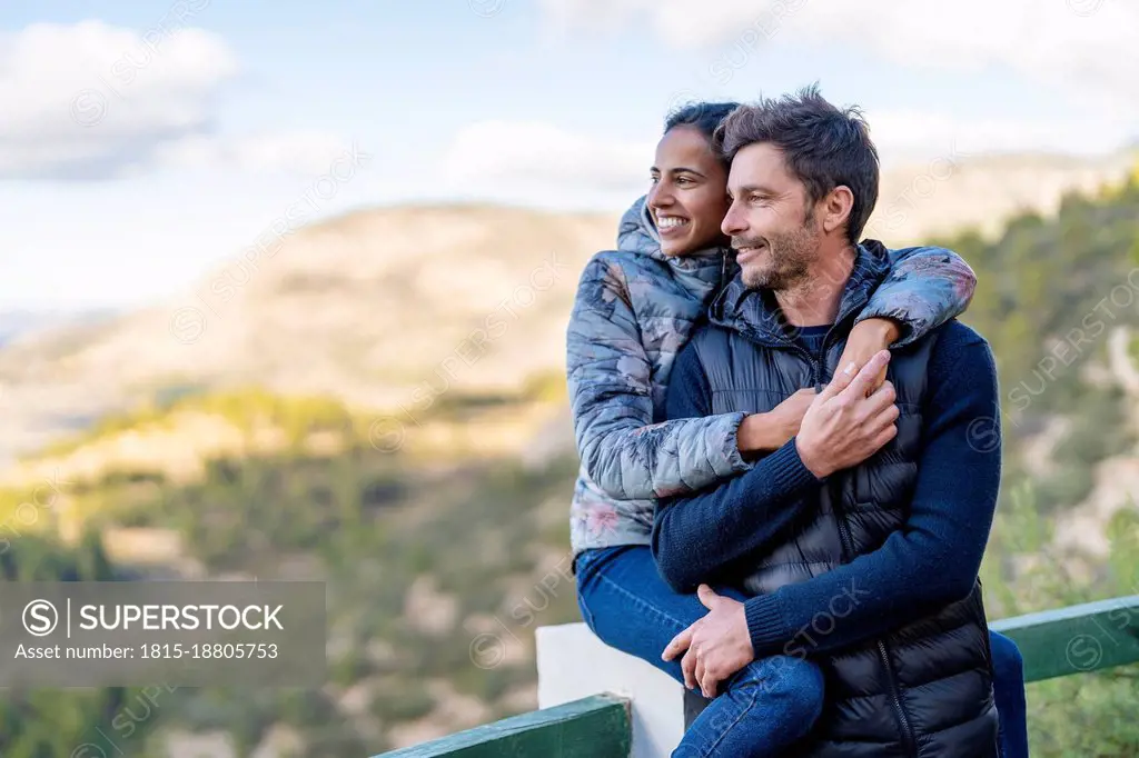 Smiling woman sitting on railing embracing man from behind at park