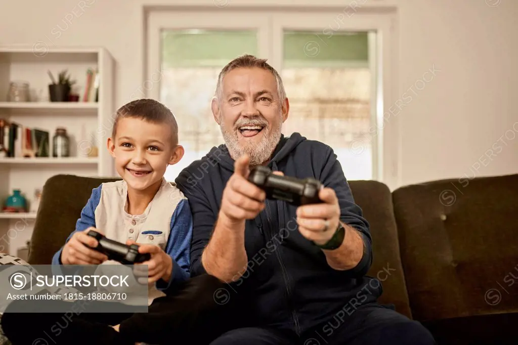 Playful grandfather playing video game with grandson at home