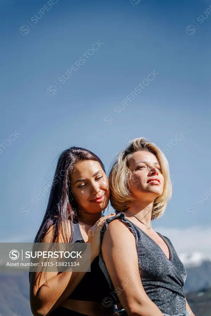 Young woman standing with blond friend under blue sky on sunny day