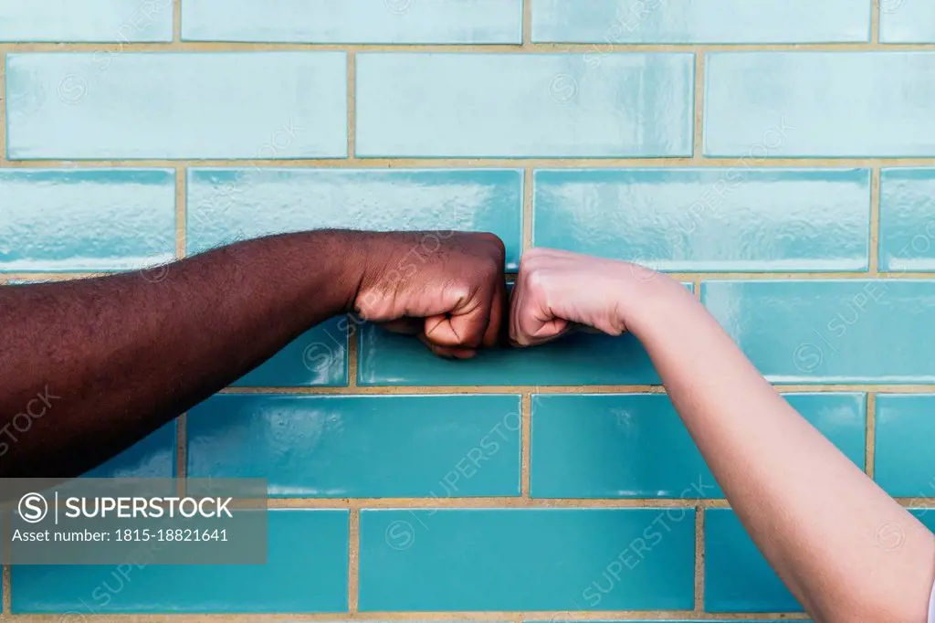 Man and woman giving fist bump on turquoise brick wall
