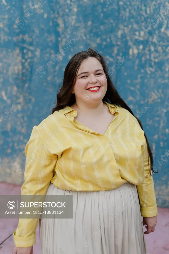 Smiling plus size woman standing in front of wall