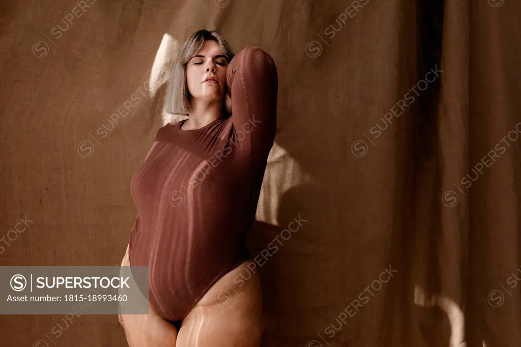 Beautiful curvy blond woman with eyes closed in front of brown backdrop