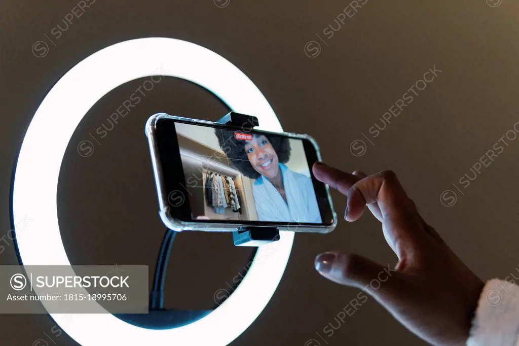 Smiling woman vlogging on smart phone in illuminated ring light