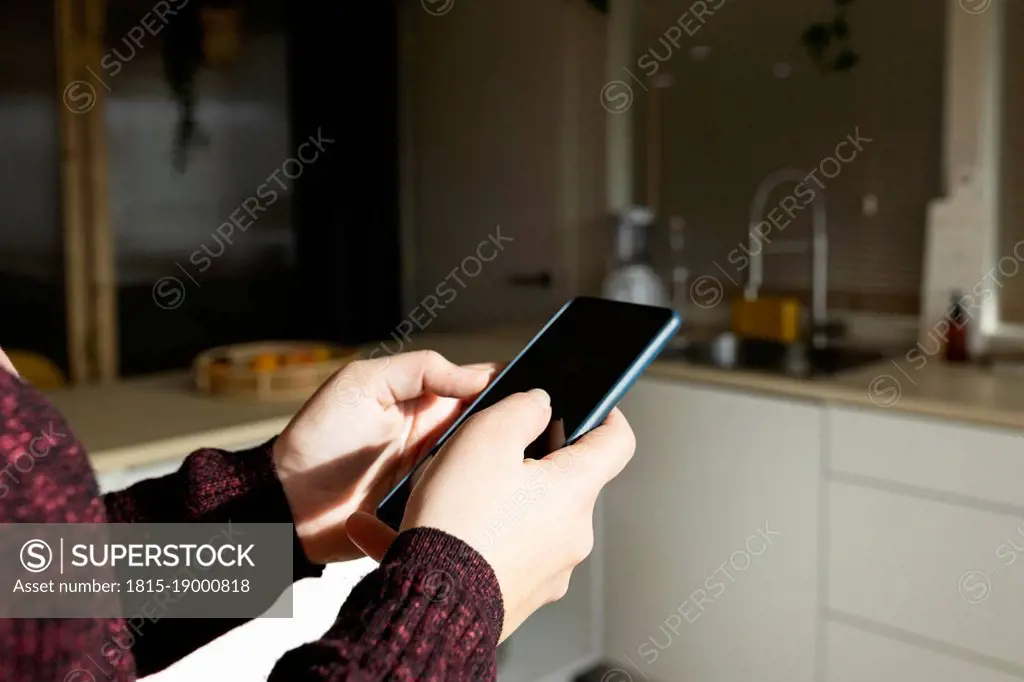 Woman using smart phone in kitchen on sunny day