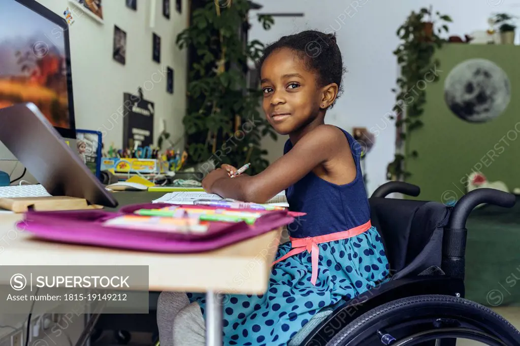 Smiling girl sitting on wheelchair and studying at home