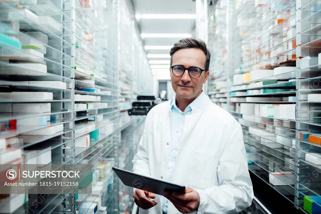 Pharmacist with tablet PC standing in storage room at pharmacy