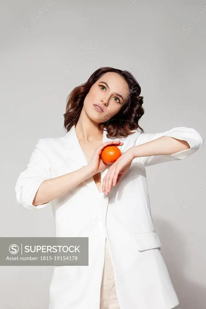 Woman holding tangerine standing against white background