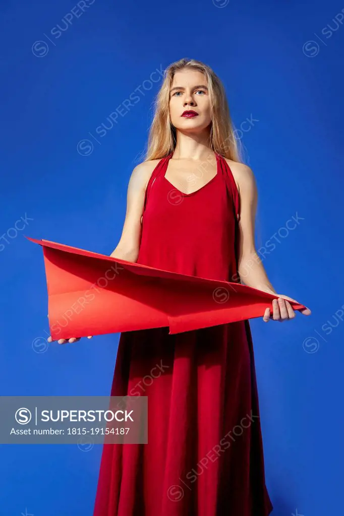 Woman holding red paper airplane standing against blue background