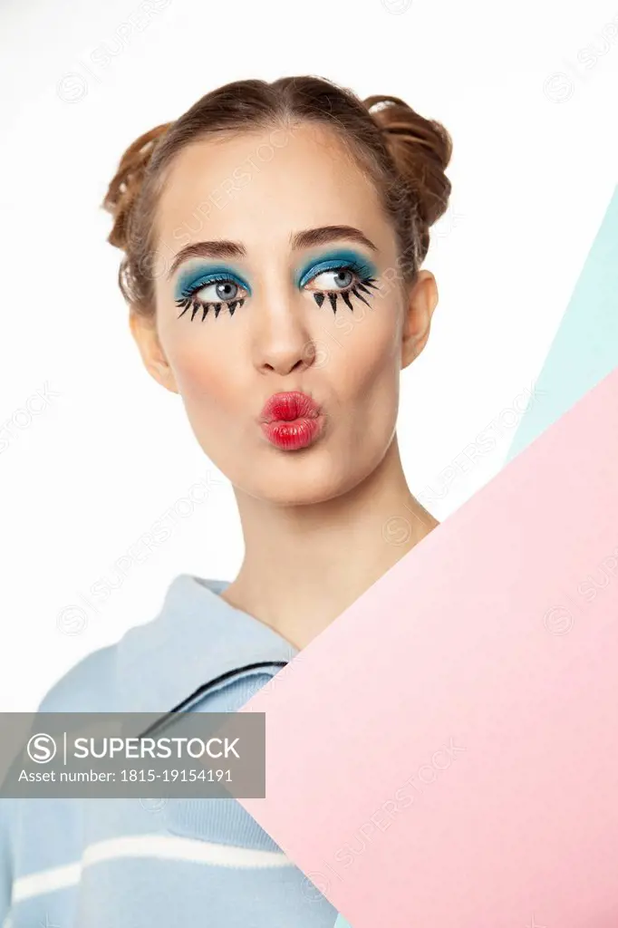 Woman with creative make-up puckering against white background