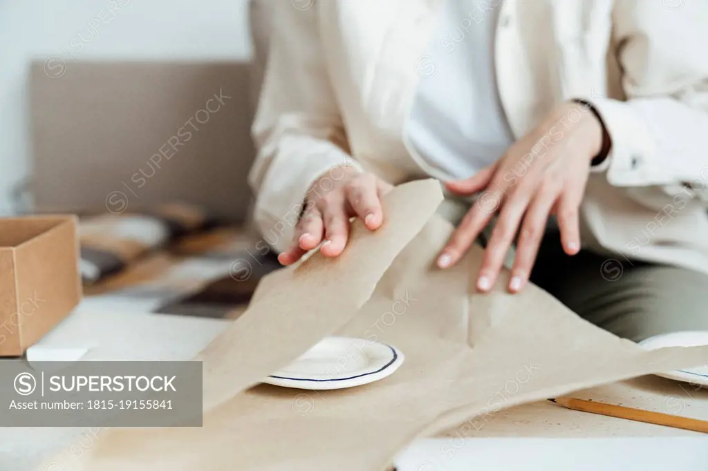 Craftswoman packing ceramic plate in wrapping paper for shipping