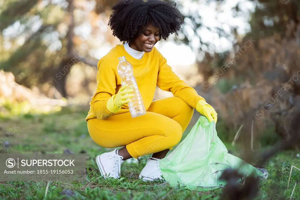 Smiling young woman picking up plastic bottle in park