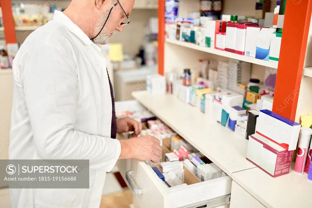 Pharmacist wearing eyeglasses opening drawer of medicines at pharmacy store