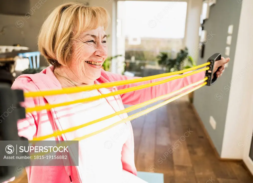 Happy senior woman doing stretching exercise with resistance band at home