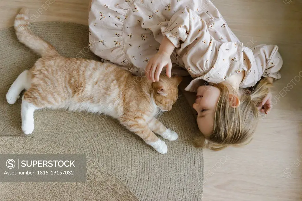 Blond girl with pet cat lying on floor at home