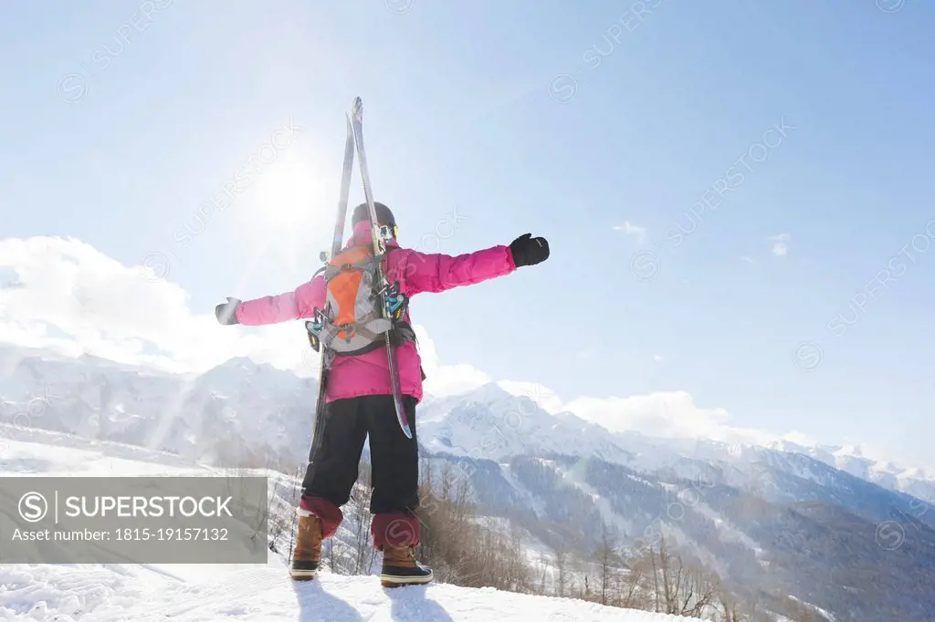 Man with backpack and ski standing with arms outstretched on snow in winter