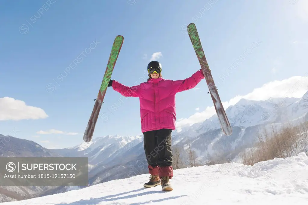 Man holding skis standing with arms outstretched on snow in winter