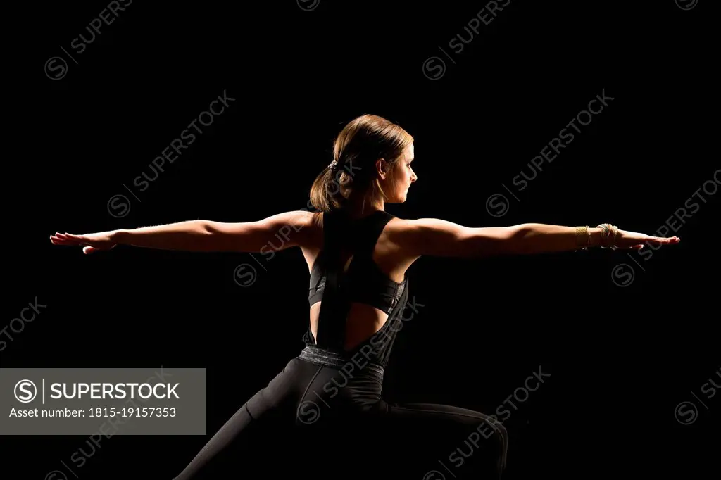 Woman with arms outstretched practicing yoga against black background