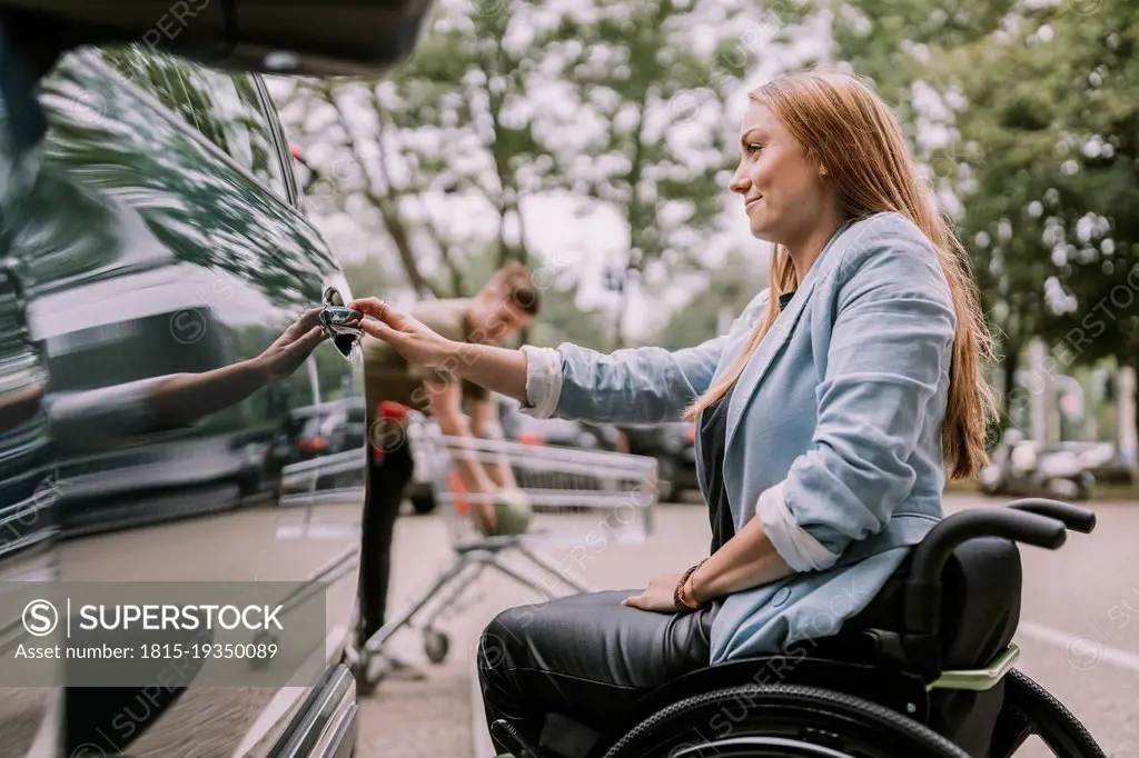 Smiling young woman sitting in wheelchair and opening car door