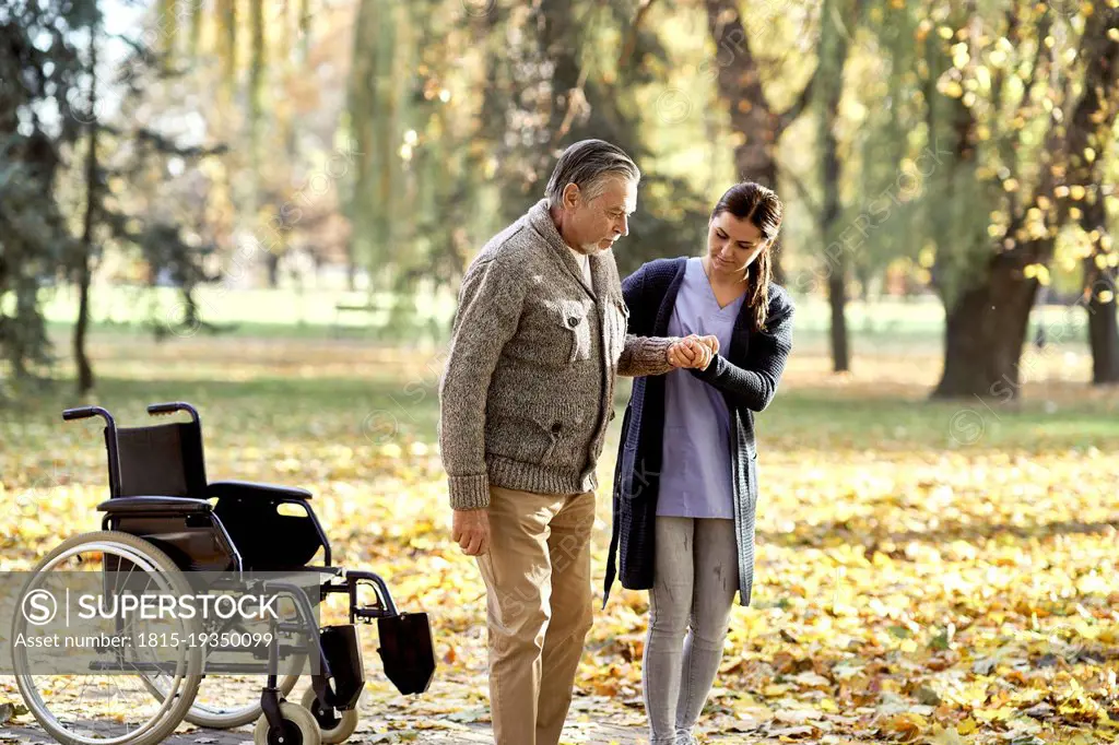 Healthcare worker helping senior disabled man walking at park