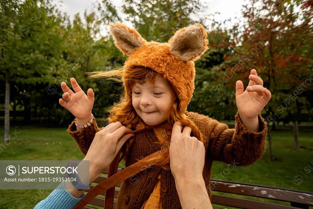 Mother tying bear costume hat of daughter at park