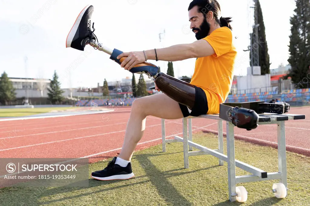 Bearded man removing prosthetic leg sitting on bench