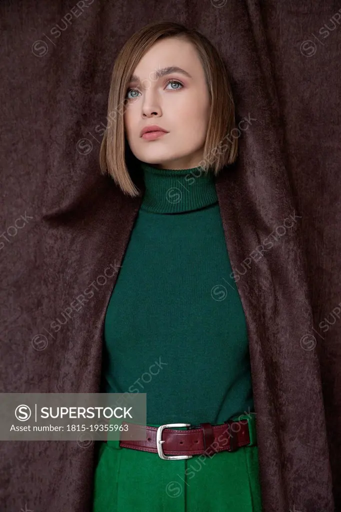 Beautiful woman in green turtleneck top standing amidst curtain