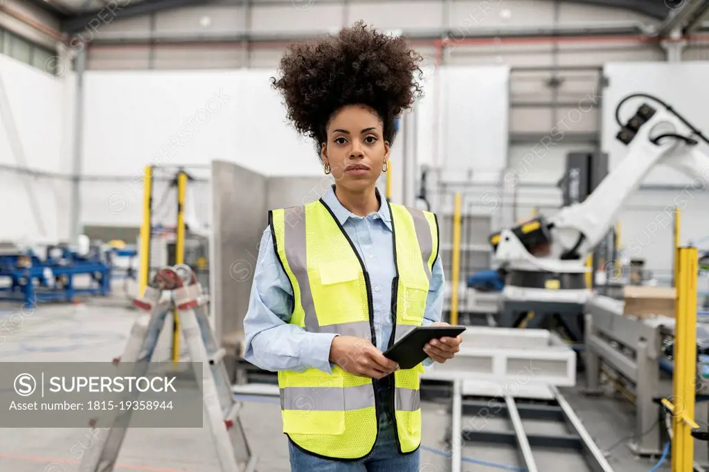 Technician holding tablet PC standing in factory